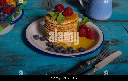 Dégustez des gaufres au caramel néerlandais avec framboises, bleuets et miel sur fond bleu en bois. Banque D'Images