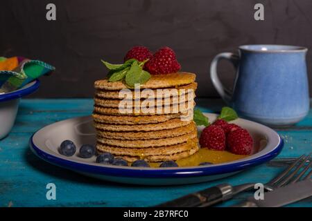 Gros plan d'une pile de gaufres néerlandaises avec framboises, bleuets et miel sur fond bleu en bois. Image isolée. Banque D'Images