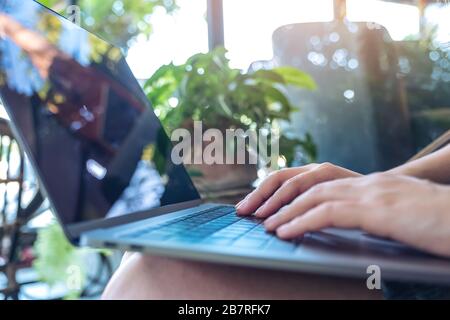 Gros plan de l'image des mains de la femme en utilisant et en tapant sur le clavier de l'ordinateur portable tout en étant assis en extérieur Banque D'Images