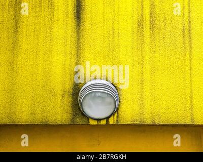 luminaire sur un mur de plâtre texturé à revêtement trame peint en jaune Banque D'Images