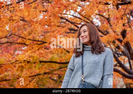 Portrait image d'une belle femme asiatique debout parmi les feuilles d'arbre de couleurs rouge et jaune en automne Banque D'Images