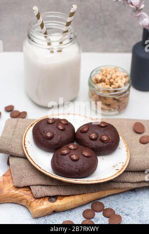 Biscuits au chocolat avec gouttes de chocolat sur la plaque blanche et verre de lait sur fond gris Banque D'Images