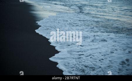 Eau blanche du Tide Rolling in et se rétraitant sur le sable de plage sombre sur la plage en Grèce dans les îles grecques Banque D'Images