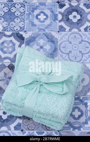 Serviettes de toilette vertes empilées flanelles attachées avec ruban et noeud. Sur une surface bleue en mosaïque à motifs Banque D'Images