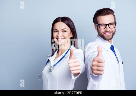Deux médecins réussis en uniforme et montrant des pouces vers le haut sur fond gris Banque D'Images