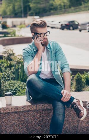 Un jeune homme à barbe rouge élégant dans un Jean décontracté est en train de parler sur son téléphone à l'extérieur. Il est à la mode et mûr Banque D'Images