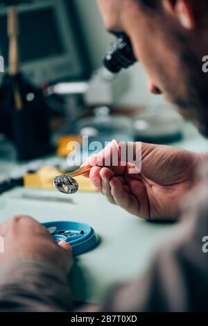 Mise au point sélective d'un horloger dans une pièce de montre de maintien de lunettes dans des brucelles par plateau d'outils sur la table Banque D'Images