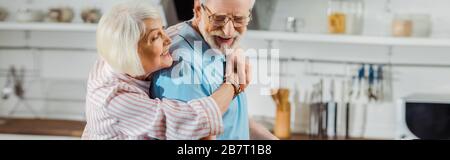 Photo panoramique d'une femme âgée embrassant un mari souriant dans la cuisine Banque D'Images