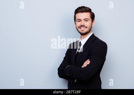 Un jeune homme souriant et souriant, habillé avec des mains croisées se tenant à moitié tourné sur fond gris Banque D'Images