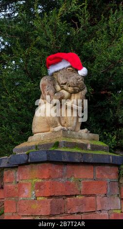 Créature en pierre sculptée avec un chapeau de Noël, sculpture de type gargouille effrayante placée sur un pilier en brique de poteau de porte à l'entrée d'une propriété Banque D'Images