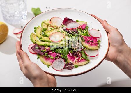 vue réduite d'une femme tenant une salade de radis frais avec des légumes verts et de l'avocat sur plaque Banque D'Images