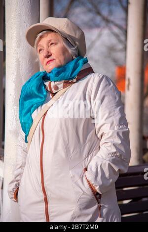 Une femme âgée penche contre une colonne du belvédère et bénéficie des rayons du soleil de printemps. Banque D'Images