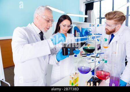 Travail d'équipe. Trois scientifiques travaillent ensemble pour de nouvelles expériences en laboratoire, tous portant des blouses, des gants et des lunettes de sécurité Banque D'Images