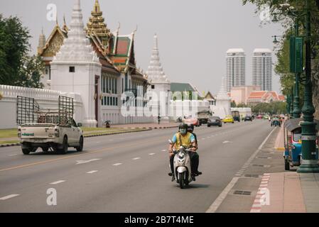 Une moto passe devant le Grand Palace avec le conducteur et le passager portant tous deux un masque de protection Banque D'Images