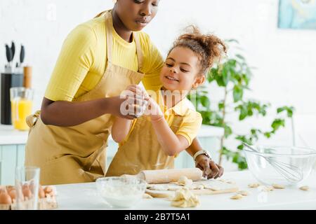 foyer sélectif de mignons gamin afro-américain tenant de la pâte crue près de la mère et des boulettes sur le tableau de découpe Banque D'Images