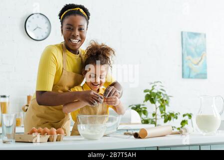 mignonne afro-américaine et belle-mère ajoutant des œufs dans le bol tout en cuisinant dans la cuisine Banque D'Images