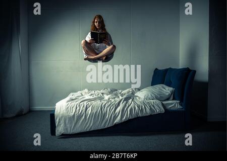 femme démoniaque dans la nuit lévitant sur le lit pendant la lecture de la bible Banque D'Images