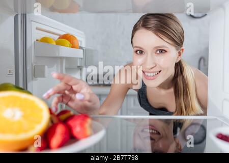 foyer sélectif de la gaie femme atteignant les fruits dans le réfrigérateur Banque D'Images