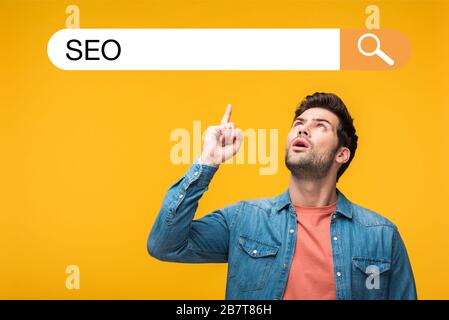 homme de poignée confus pointant avec doigt sur l'illustration de la barre de recherche avec lettrage seo isolé sur le jaune Banque D'Images