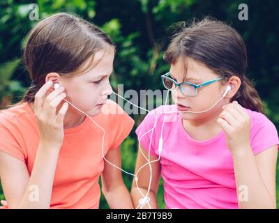 Les filles partageant un casque pour écouter de la musique. Des amis heureux passent du temps ensemble. Banque D'Images