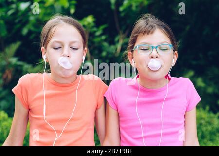 Les filles partageant un casque pour écouter de la musique. Les sœurs mâcher la gomme et en faire des ballons. Des amis heureux passent du temps ensemble Banque D'Images