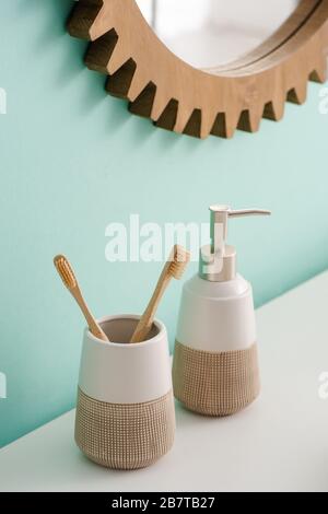 Porte-brosse à dents avec brosses à dents et savon liquide près du miroir rond sur le mur dans la salle de bains, concept zéro déchet Banque D'Images