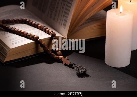 sainte bible avec rosaire sur fond noir sombre avec bougies brûlantes Banque D'Images