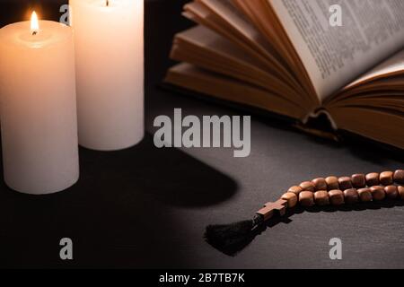 sainte bible avec rosaire sur fond noir sombre avec bougies brûlantes Banque D'Images