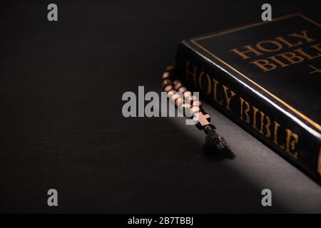 sainte bible avec rosaire sur fond noir sombre avec bougies brûlantes Banque D'Images