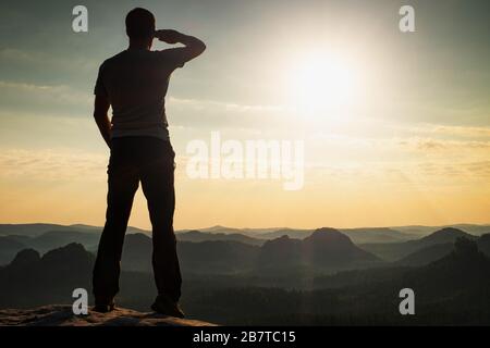 Homme haut à bras levé pour observer les yeux restent sur le sommet de la falaise de montagne en face du ciel lumineux coucher de soleil profitant de la liberté et pure na Banque D'Images