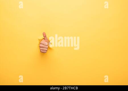 vue rognée de l'homme montrant le pouce à travers le trou de papier jaune Banque D'Images