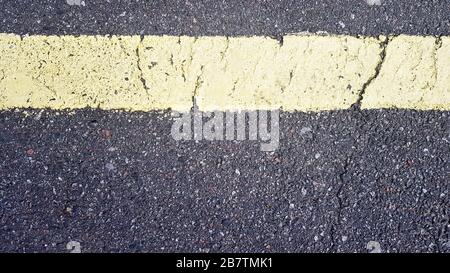bande horizontale jaune sur asphalte. Détail d'une bande jaune usée avec le temps avec une fissure, marquage de route sur l'asphalte. Banque D'Images