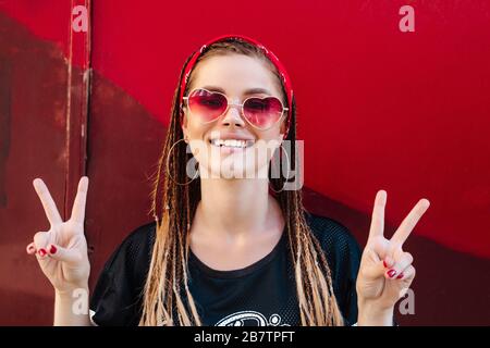 Cool hipster étudiant femme portant des lunettes de soleil et bandana rouge souriant heureux sur la rue de la ville . Banque D'Images