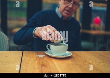 Un homme mûr dans un café verse du lait dans son café et le répand sur la table Banque D'Images