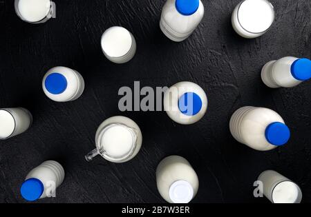 Emballage des produits laitiers, bouteilles et verres avec lait sur fond noir, vue du dessus Banque D'Images