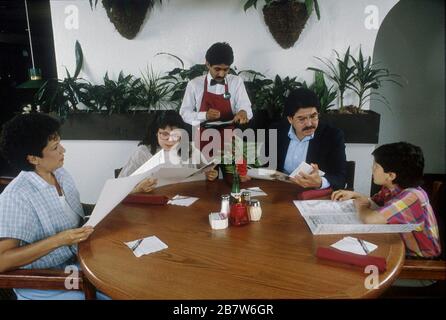 Austin, Texas États-Unis : les membres de la famille hispanique regardent les menus et commandent auprès du serveur tout en dînant au restaurant italien. M. ©Bob Daemmrich Banque D'Images