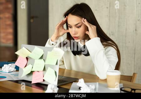 Difficultés de travail. Femme tenant la tête, devant l'ordinateur portable Banque D'Images