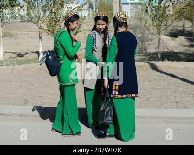 Trois jeunes filles étudiantes avec des tresses portant une robe nationale turkmène utilisée comme uniforme scolaire à Kunya Urgench. Robe longue verte et chapeau de tekke. Banque D'Images
