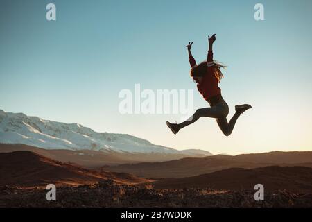 Une jeune fille heureuse saute contre les montagnes et le coucher du soleil Banque D'Images