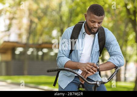 Suivi de la forme physique. Beau homme africain sur le vélo regardant sa Smartwatch Banque D'Images