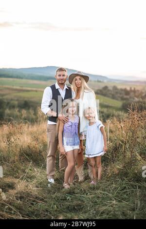 Portrait d'une famille heureuse avec des enfants portant des vêtements boho de cowboy élégants debout dans le champ de campagne et regardant l'appareil photo. Coucher de soleil d'été sur le terrain Banque D'Images