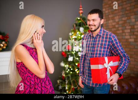 Un jeune homme positif donne à sa belle jolie femme un cadeau dans une boîte pour le nouvel an. Concept cadeau pour votre deuxième moitié. Concept de promotions et de réductions Banque D'Images