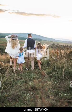 Regardez à l'arrière la photo d'une famille joyeuse dans des vêtements tendance élégants, des parents et des enfants, en profitant et en courant ensemble dans les montagnes. Famille dans Banque D'Images