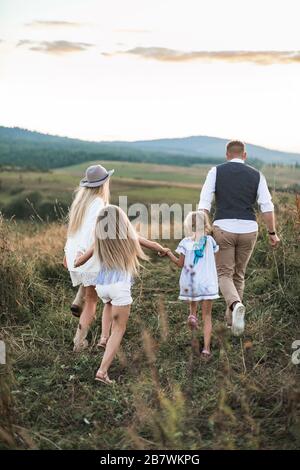 Mère et père jouant avec leurs enfants filles sur le terrain, courir et rire, vue arrière. Concept de style de vie de famille heureux. Banque D'Images