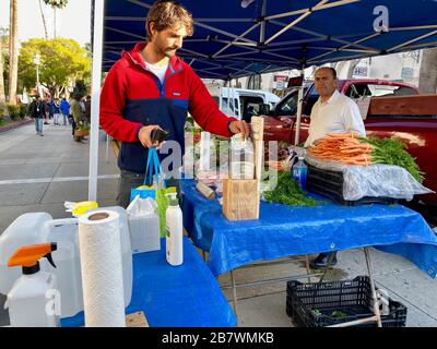 17 mars 2020, Santa Barbara, Californie, États-Unis : un homme se lave les mains et fait un don au Farmer-Vendor qui a mis en place et fourni la station de lavage des mains. Malgré la peur du virus Corona, les habitants et les touristes de Santa Barbara viennent sur le marché du mardi soir de FarmerÃs le 17 mars 2020 pour faire des achats de fleurs fraîches coupées, de légumes biologiques, d'herbe de blé, de viandes nourries d'herbe, de miel, d'huiles d'olive, etc. Beaucoup semble normal, mais la vue des gants bleus, des masques, des machines à laver les mains et des postes à laver les mains à changement de vitesse, ainsi que la présence peu intense pour le marché habituellement animé, révèlent quelque chose Banque D'Images