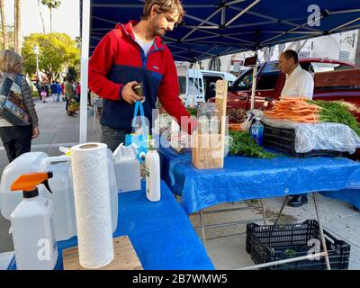 17 mars 2020, Santa Barbara, Californie, États-Unis : un homme se lave les mains et fait un don au Farmer-Vendor qui a mis en place et fourni la station de lavage des mains. Malgré la peur du virus Corona, les habitants et les touristes de Santa Barbara viennent sur le marché du mardi soir de FarmerÃs le 17 mars 2020 pour faire des achats de fleurs fraîches coupées, de légumes biologiques, d'herbe de blé, de viandes nourries d'herbe, de miel, d'huiles d'olive, etc. Beaucoup semble normal, mais la vue des gants bleus, des masques, des machines à laver les mains et des postes à laver les mains à changement de vitesse, ainsi que la présence peu intense pour le marché habituellement animé, révèlent quelque chose Banque D'Images