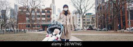 Mère caucasienne en masque chirurgical marchant avec bébé en plein air à Toronto. Masque protecteur contre la pneumonie chinoise COVID-19 épidémie de virus maladie Banque D'Images