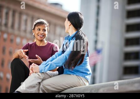 Two smiling women having a conversation, alors qu'il était assis dans un parc de la ville. Banque D'Images