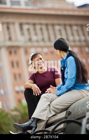Two smiling women having a conversation, alors qu'il était assis dans un parc de la ville. Banque D'Images