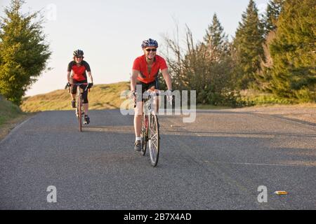 Deux femmes ensemble, souriant à vélo le long d'une route de campagne. Banque D'Images